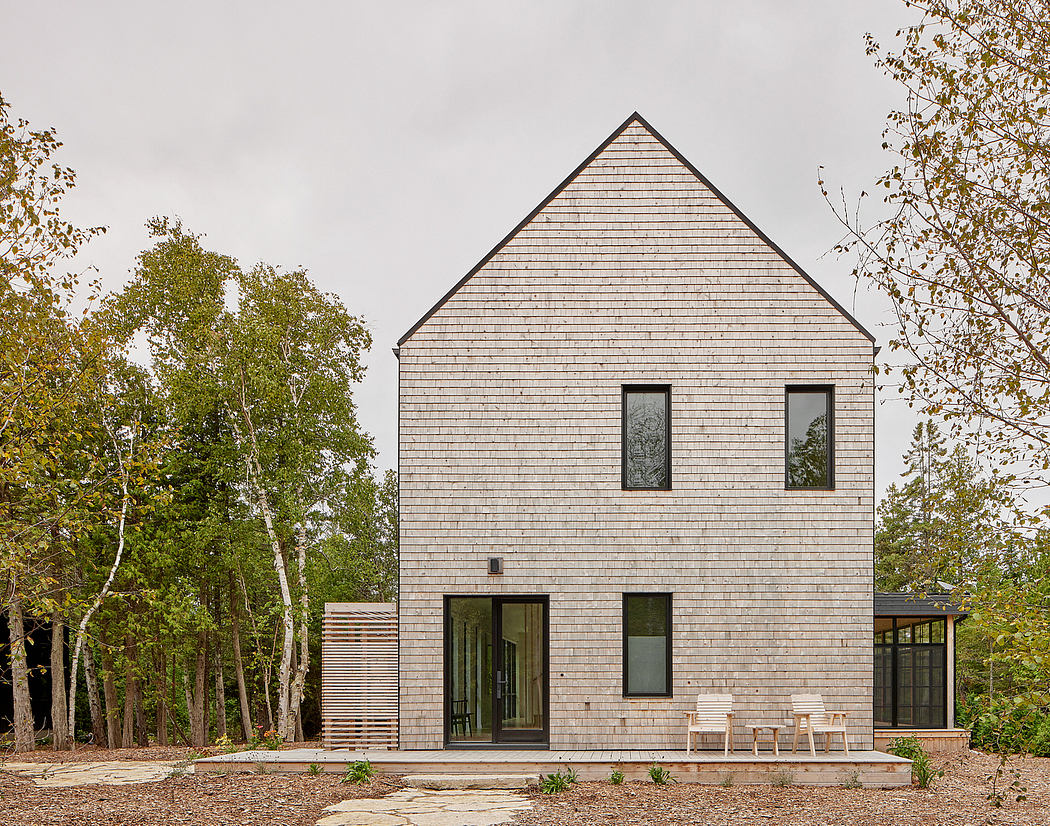 A modern, two-story wooden-shingled house surrounded by lush greenery.
