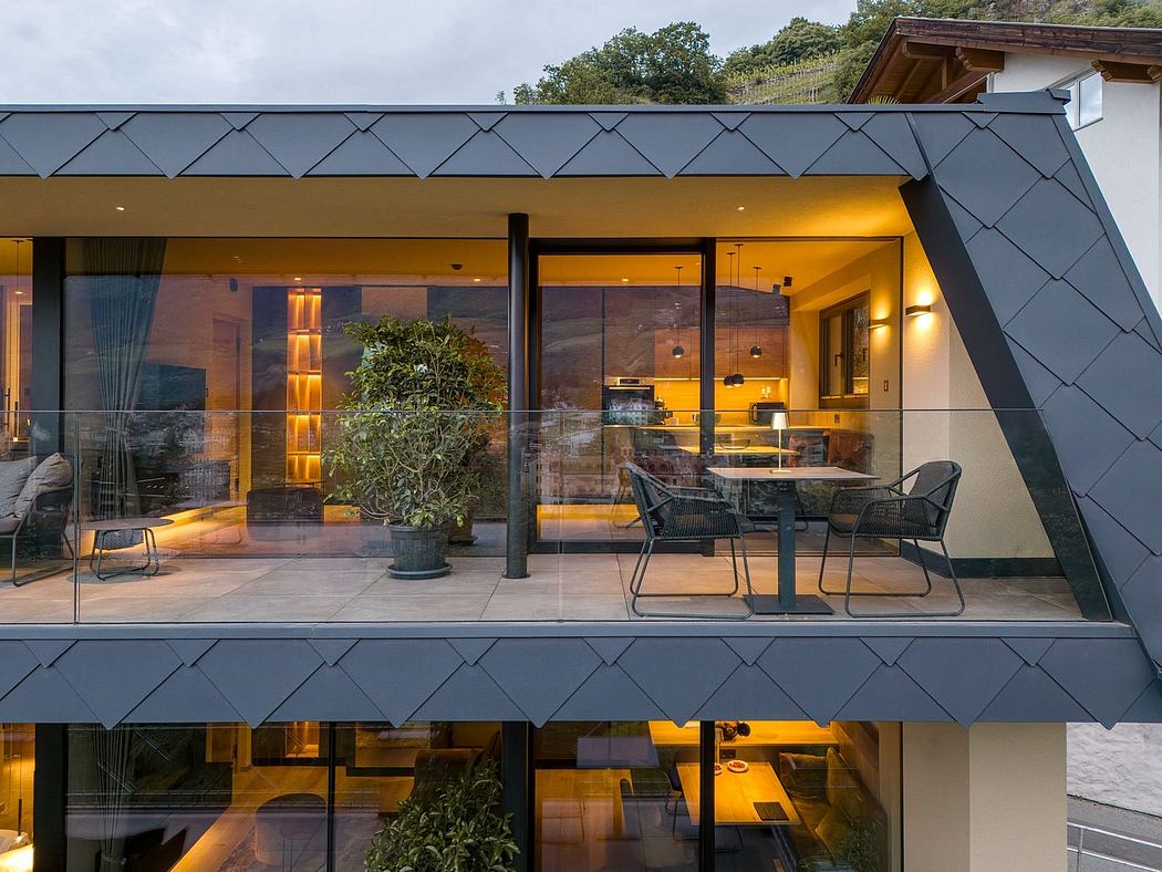 Modern mountain lodge with slate roof, floor-to-ceiling glass walls, and warm, cozy interior.