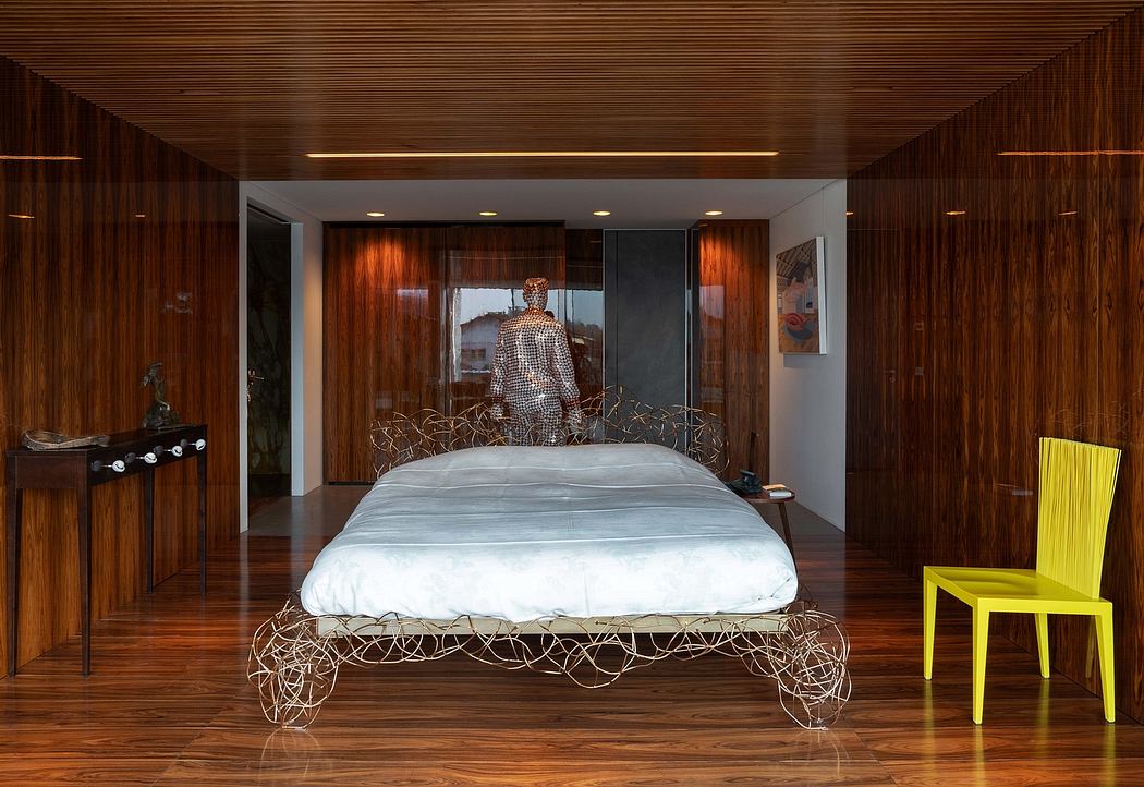 A modern, wooden-paneled bedroom with a sculptural wire bed frame and a vibrant yellow chair.