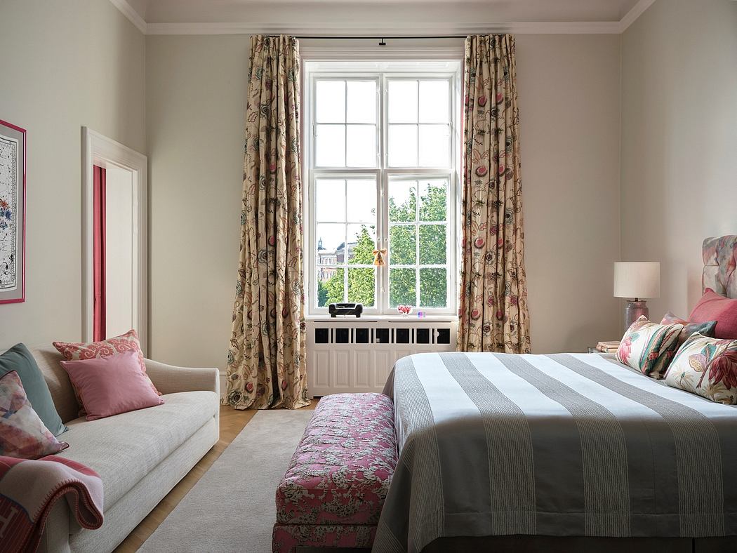 Cozy bedroom with patterned curtains, plush furnishings, and a large window overlooking greenery.