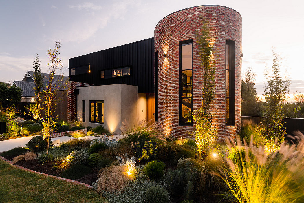 Modern brick and glass house with lush landscaping and exterior lighting.