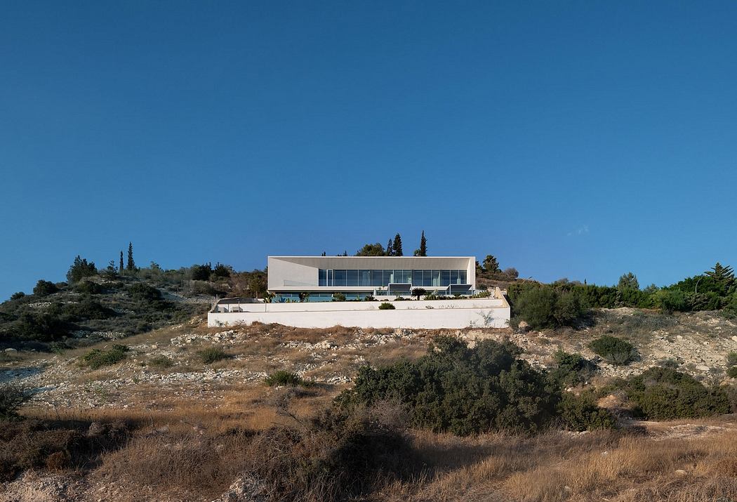 Modern, minimalist villa on a hillside with large glass windows and a swimming pool.