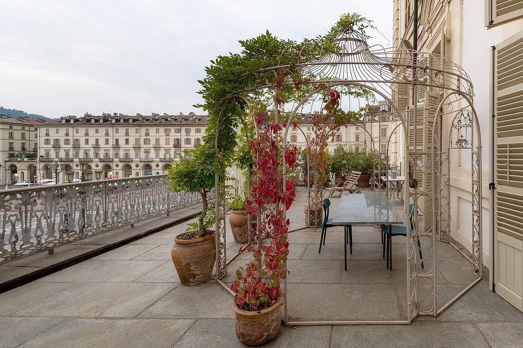 Ornate wrought-iron gazebo, terrace overlooking city square, potted plants and flowers.