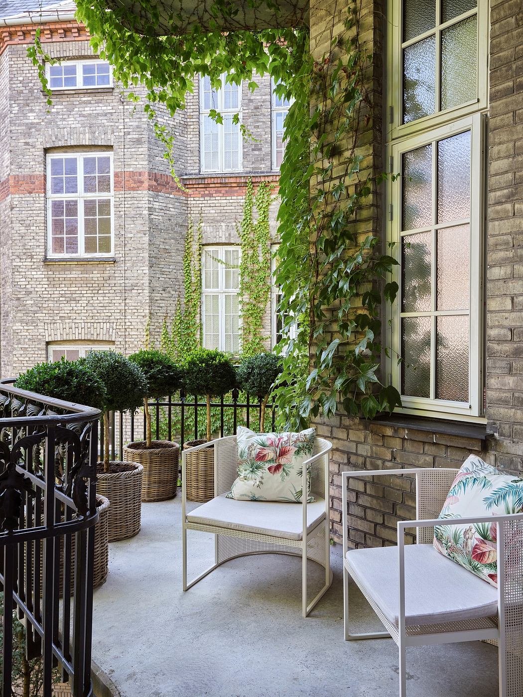 A cozy patio with wrought-iron furniture, surrounded by ivy-covered brick walls and windows.