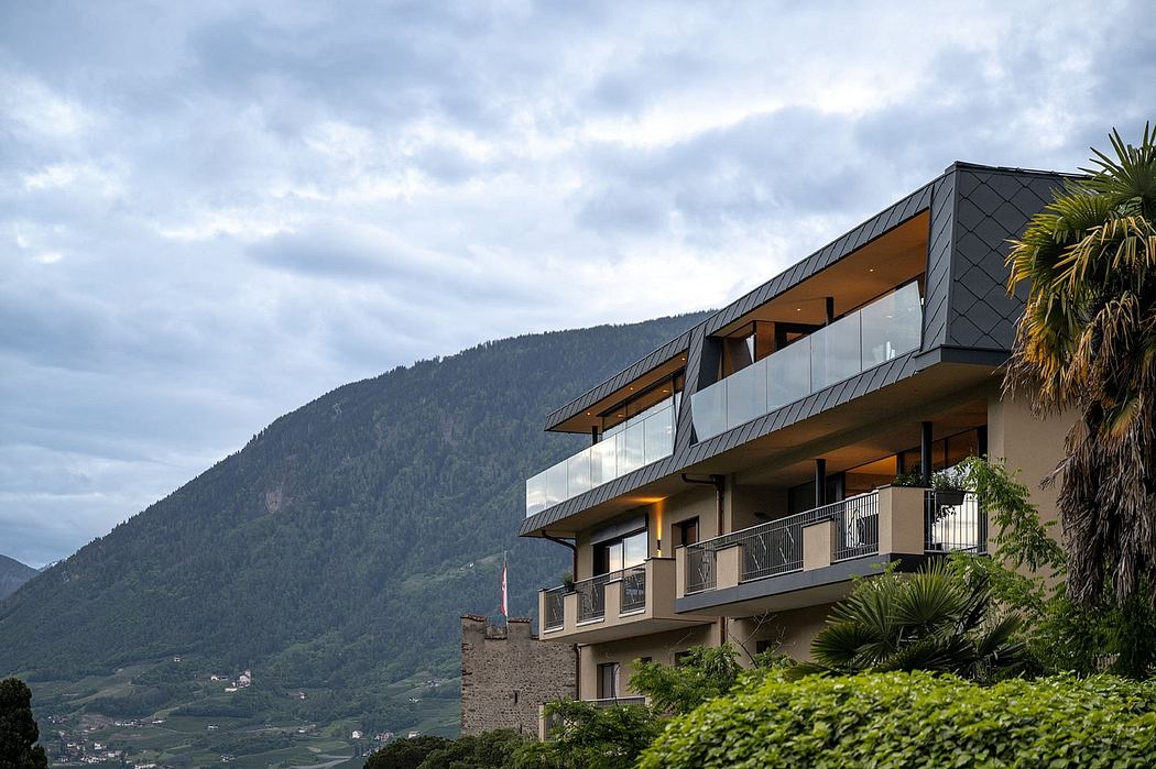 Sleek, modern architecture with angled roofs, glass walls, and balconies overlooking lush greenery and mountains.