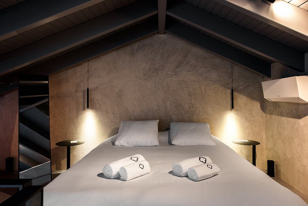 A cozy bedroom with a vaulted ceiling, concrete walls, and minimalist lighting fixtures.