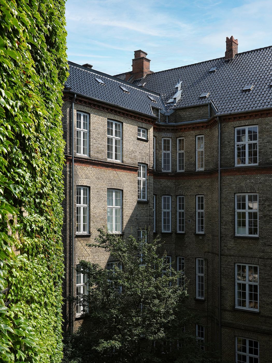 Elegant brick and stone facade with ornate windows, pitched slate roof, and lush greenery.