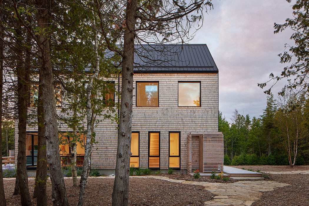 A modern, wooden-clad house nestled among trees, featuring large windows and a slanted roof.
