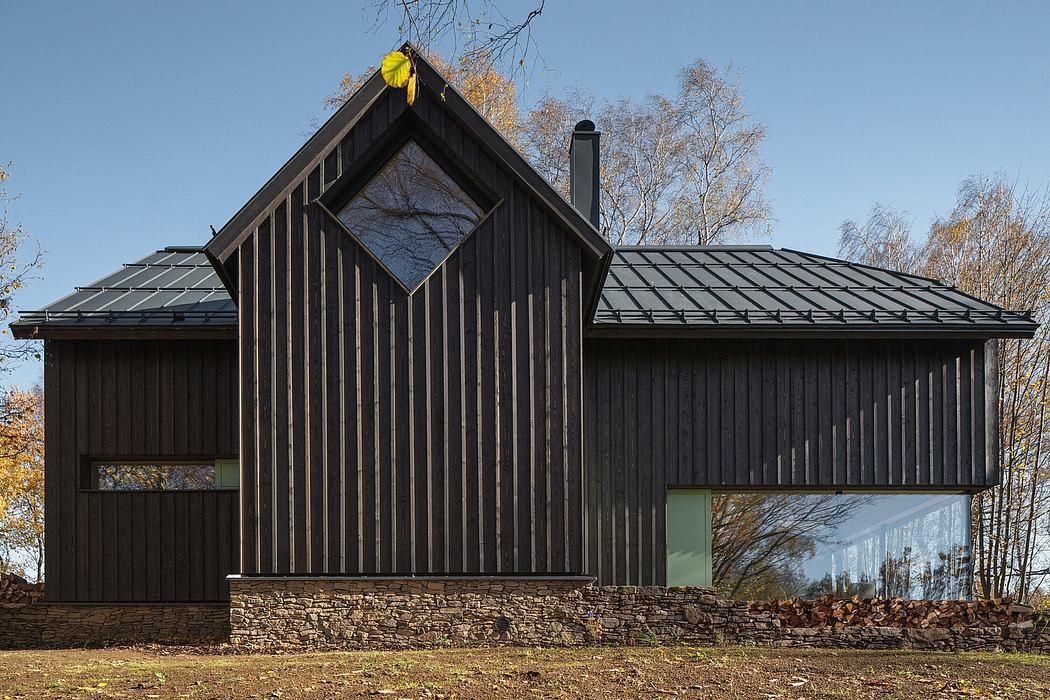 A modern, dark-colored wooden cabin with a triangular roof and large glass windows.