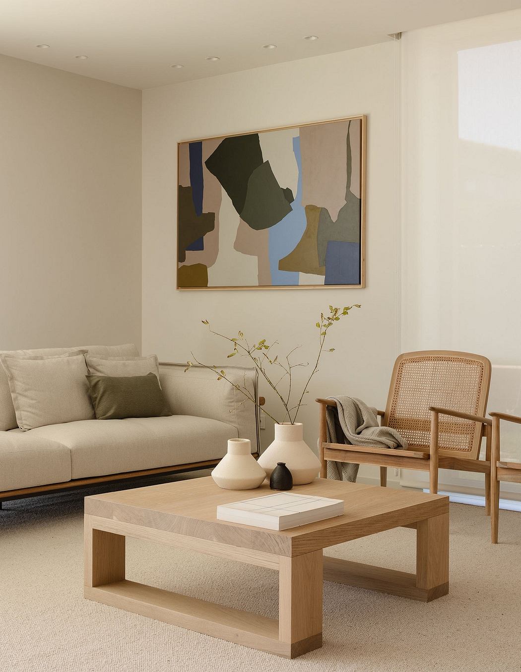 A minimalist living room with a wooden coffee table, neutral-toned sofa, and abstract art.