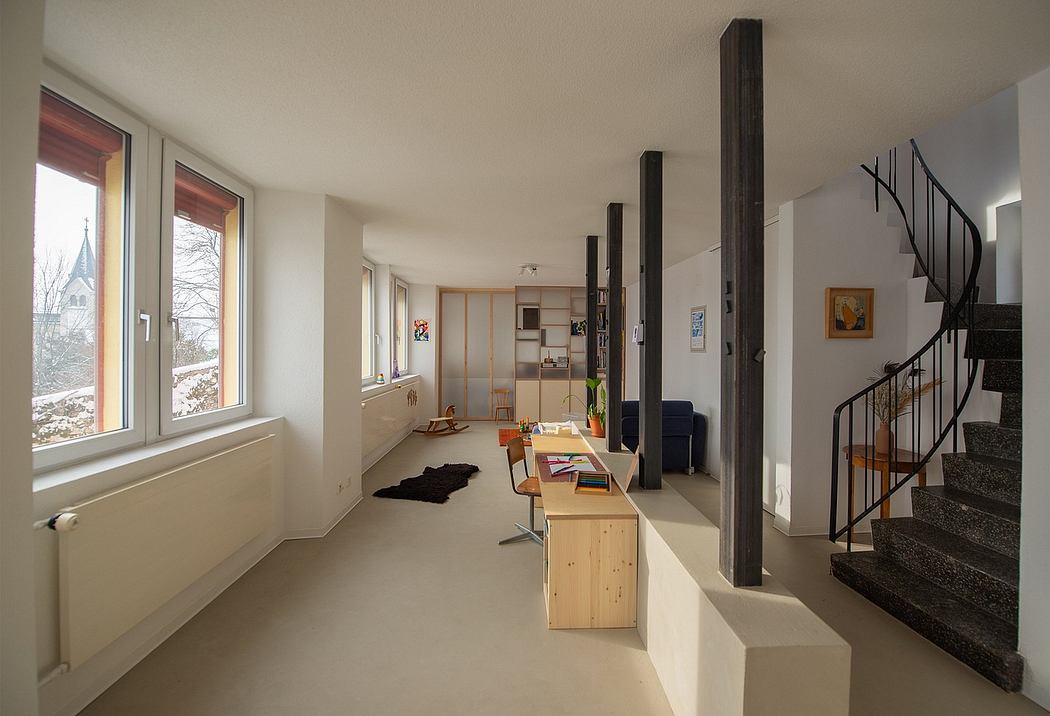 Minimalist open-concept living space with wooden accents, spiral staircase, and large windows.