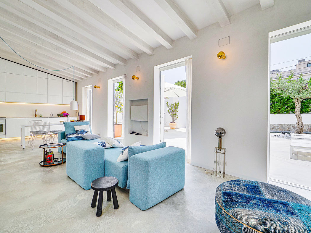 Modern open-plan living space with light-colored wood beams, large windows, and blue upholstered furniture.