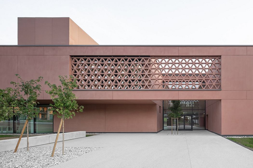A modern building with a striking geometric lattice facade, surrounded by trees and a paved courtyard.