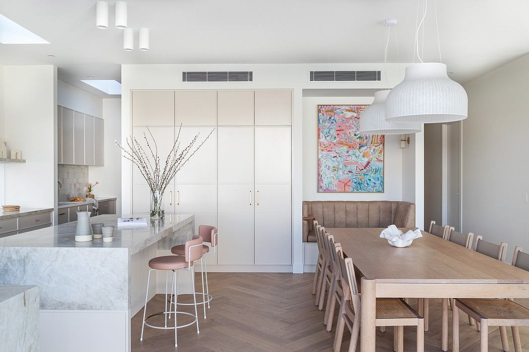 Modern kitchen and dining area with sleek white cabinets, colorful artwork, and stylish furnishings.
