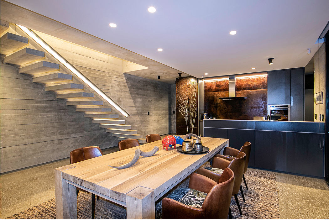 Striking concrete stairway, wooden dining table, and industrial-style kitchen in modern home.