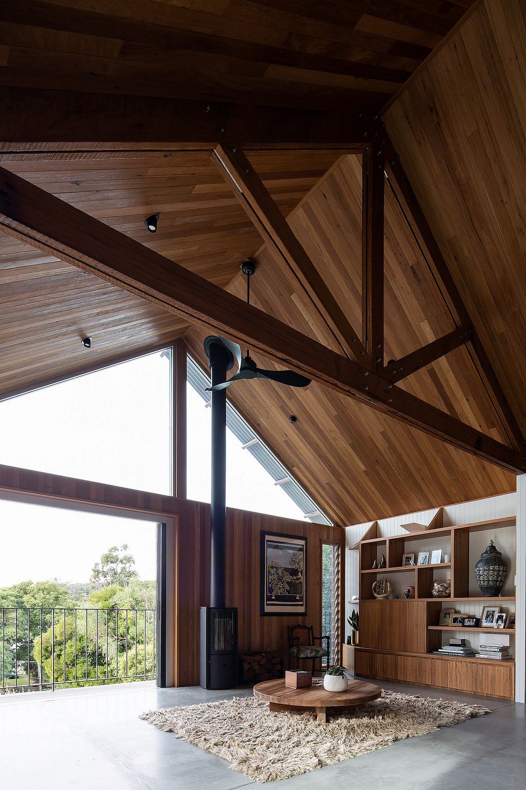 Warm, cozy living room with wooden beams, shelves, and large windows showcasing outdoor view.