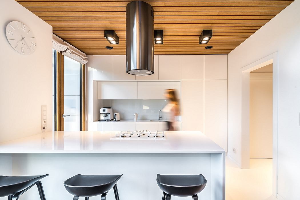 A modern, minimalist kitchen with a wooden ceiling, sleek white cabinets, and a stainless steel range hood.