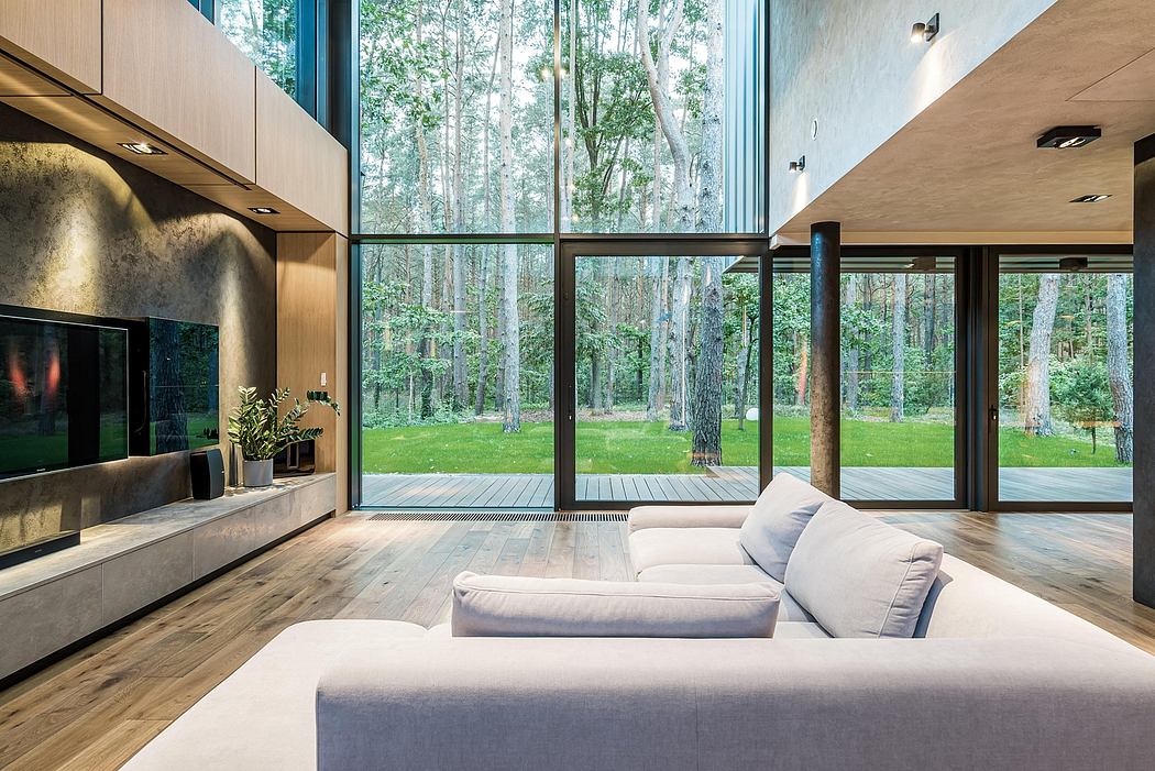 Expansive glass walls frame a verdant forest, showcasing modern, minimalist interior.