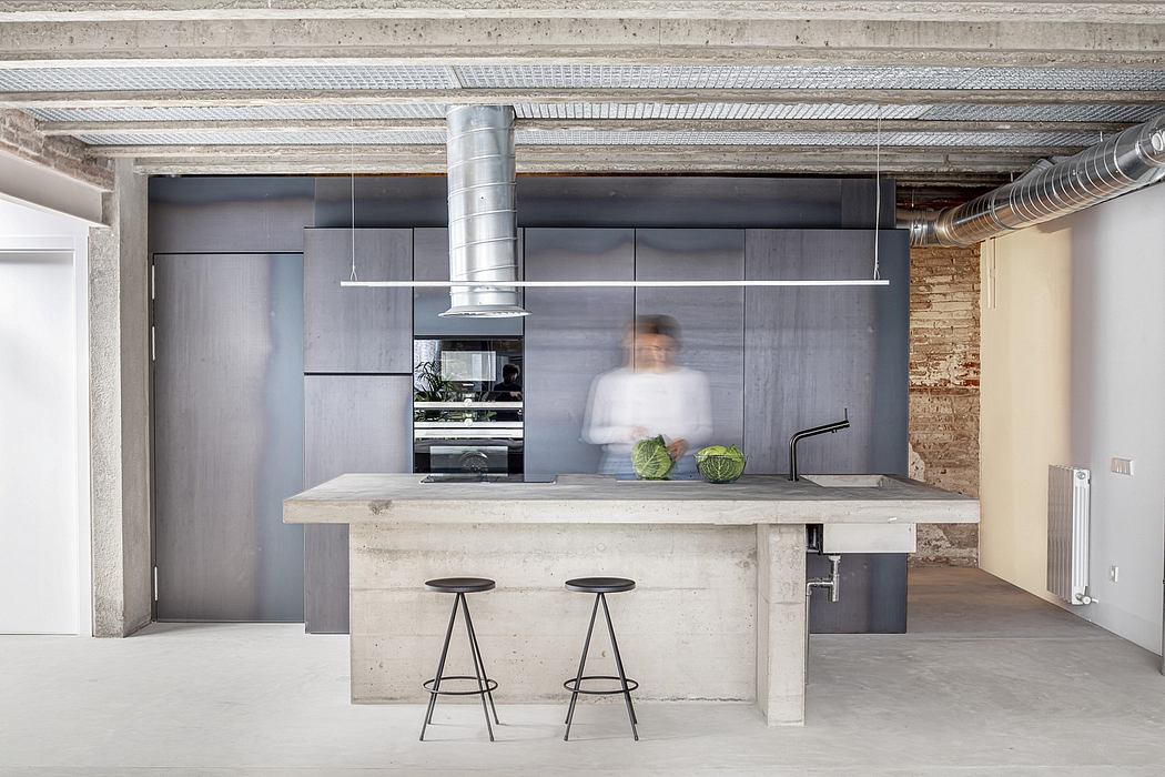 Modern industrial-style kitchen with concrete counter, steel appliances, and blurred figure.