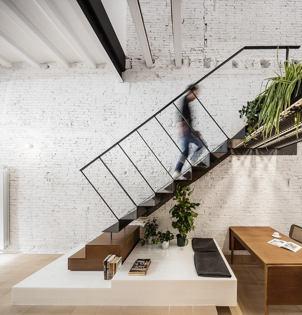 An open-concept interior with a modern steel staircase, wooden furniture, and brick walls.