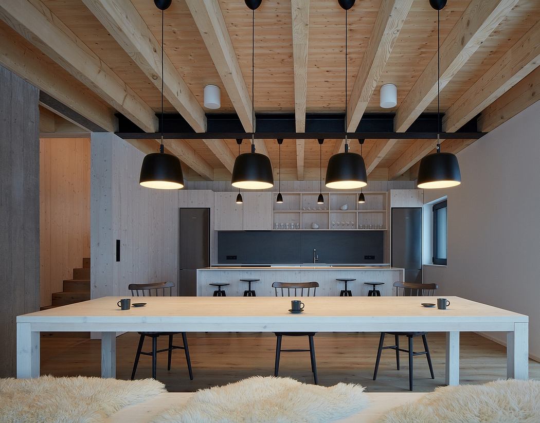 A modern, rustic-inspired kitchen and dining space with exposed wooden beams, pendant lighting, and an expansive wooden dining table.