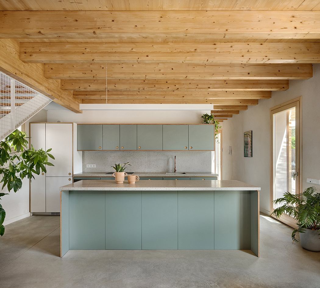 Modern kitchen with wood-beamed ceiling, mint green cabinets, and concrete flooring.