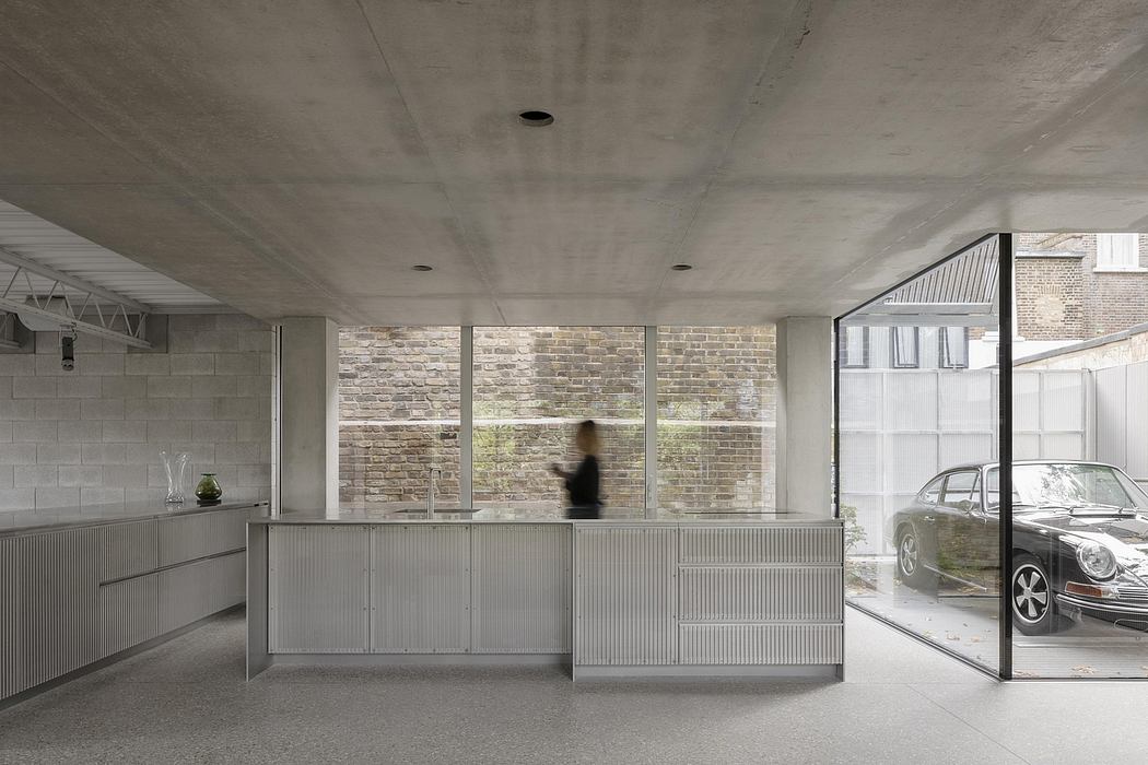 A minimalist concrete and brick interior with a blurred figure and a car visible through a glass wall.