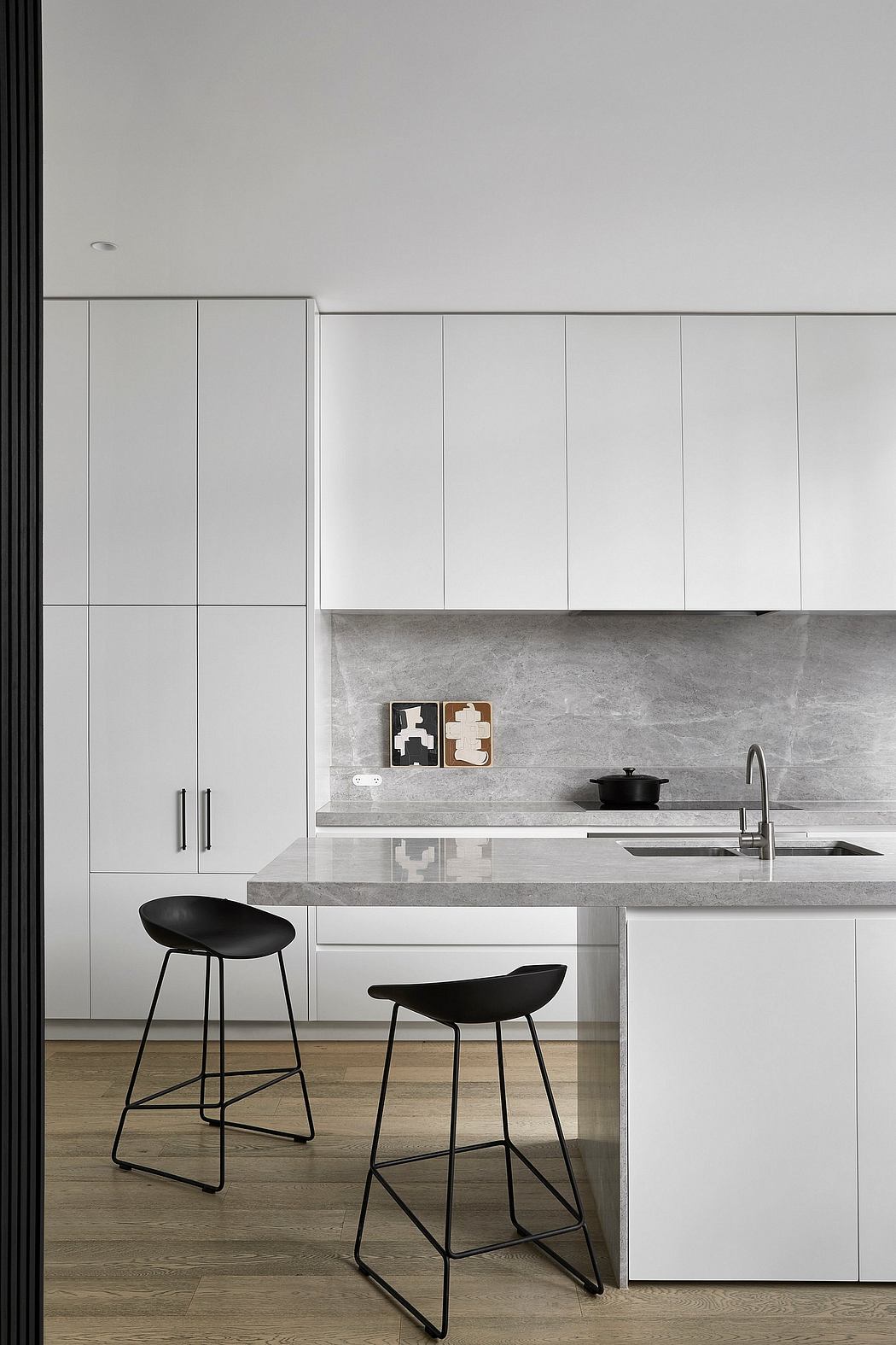 Modern minimalist kitchen with sleek white cabinets, concrete countertops, and black bar stools.