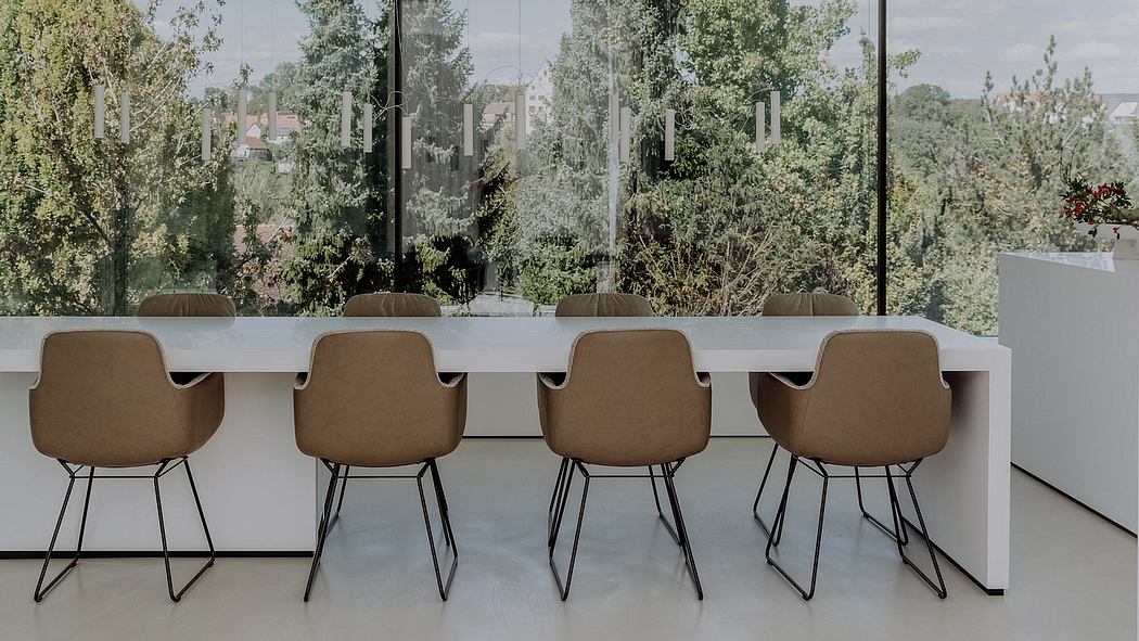 Modern minimalist dining space with a long white table and beige upholstered chairs.