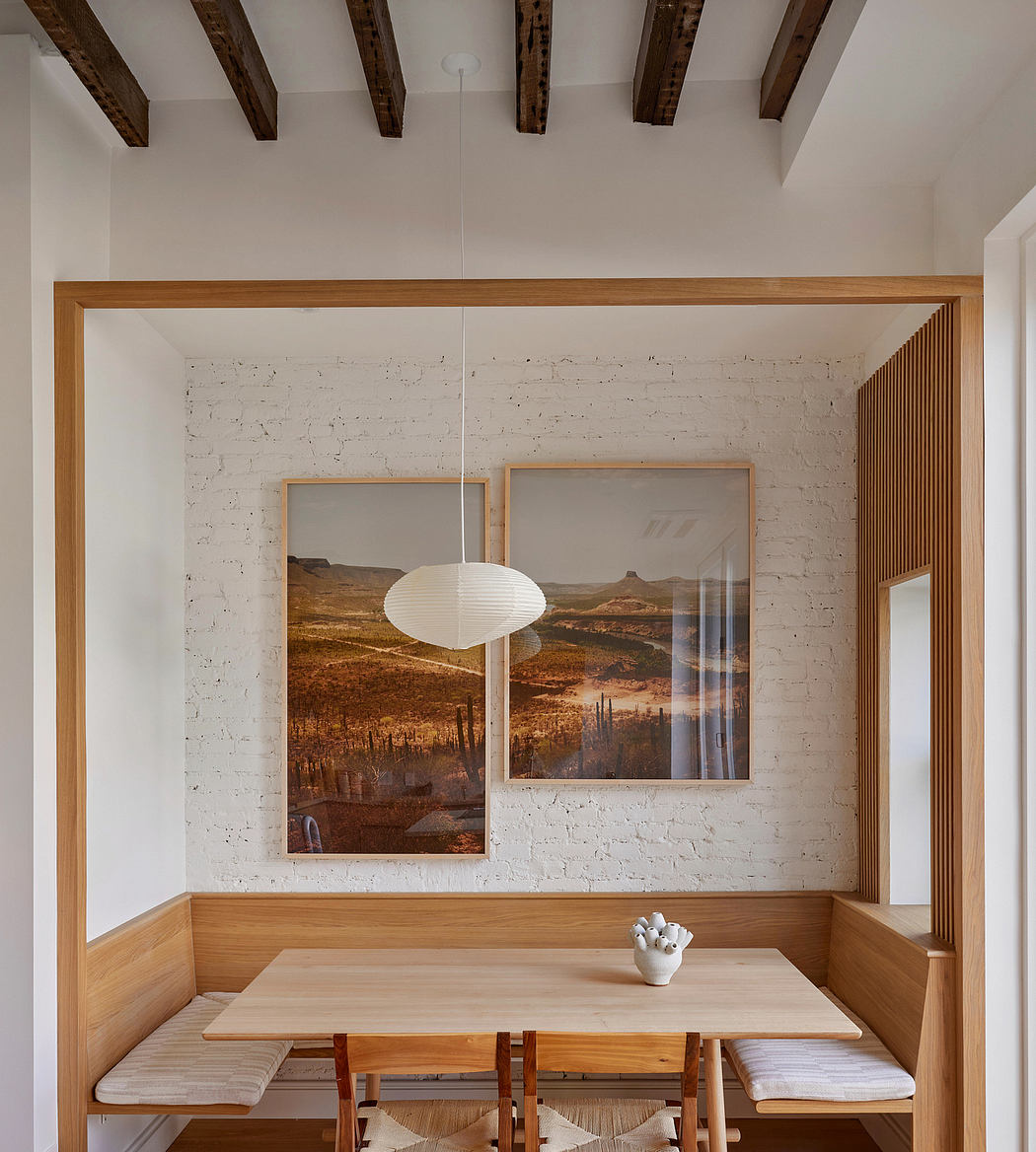 Rustic dining area with exposed wood beams, white brick wall, and landscape artwork.
