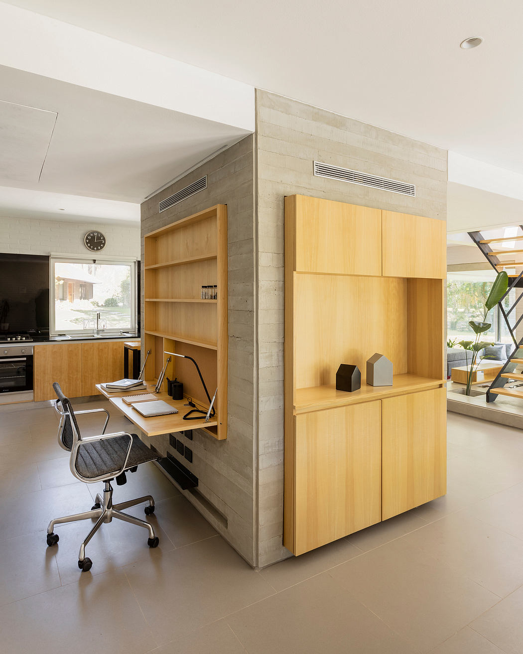 A modern work nook with concrete walls, wooden cabinetry, and a swivel chair.