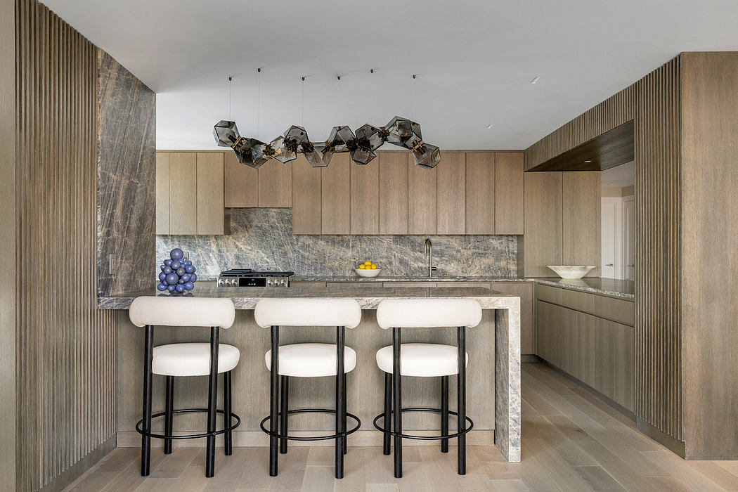 Modern kitchen with sleek gray stone countertop, geometric light fixtures, and white bar stools.