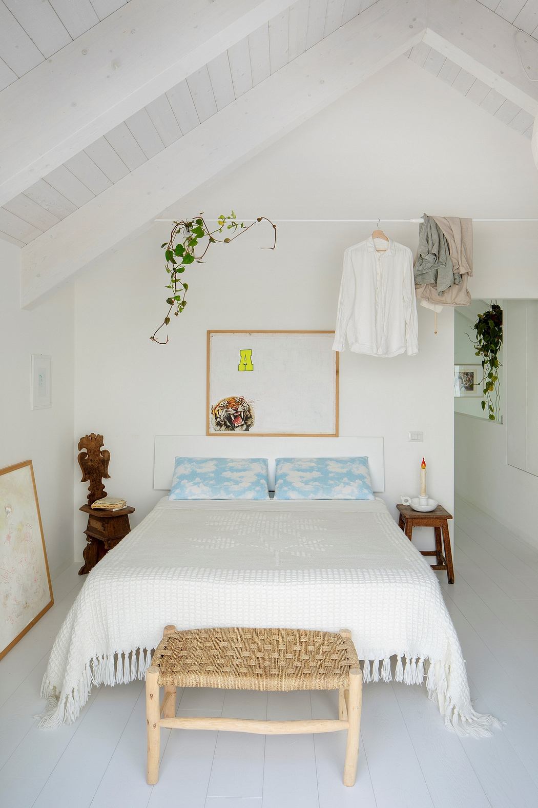 Cozy attic bedroom with white walls, wood accents, and hanging plants creating a serene atmosphere.