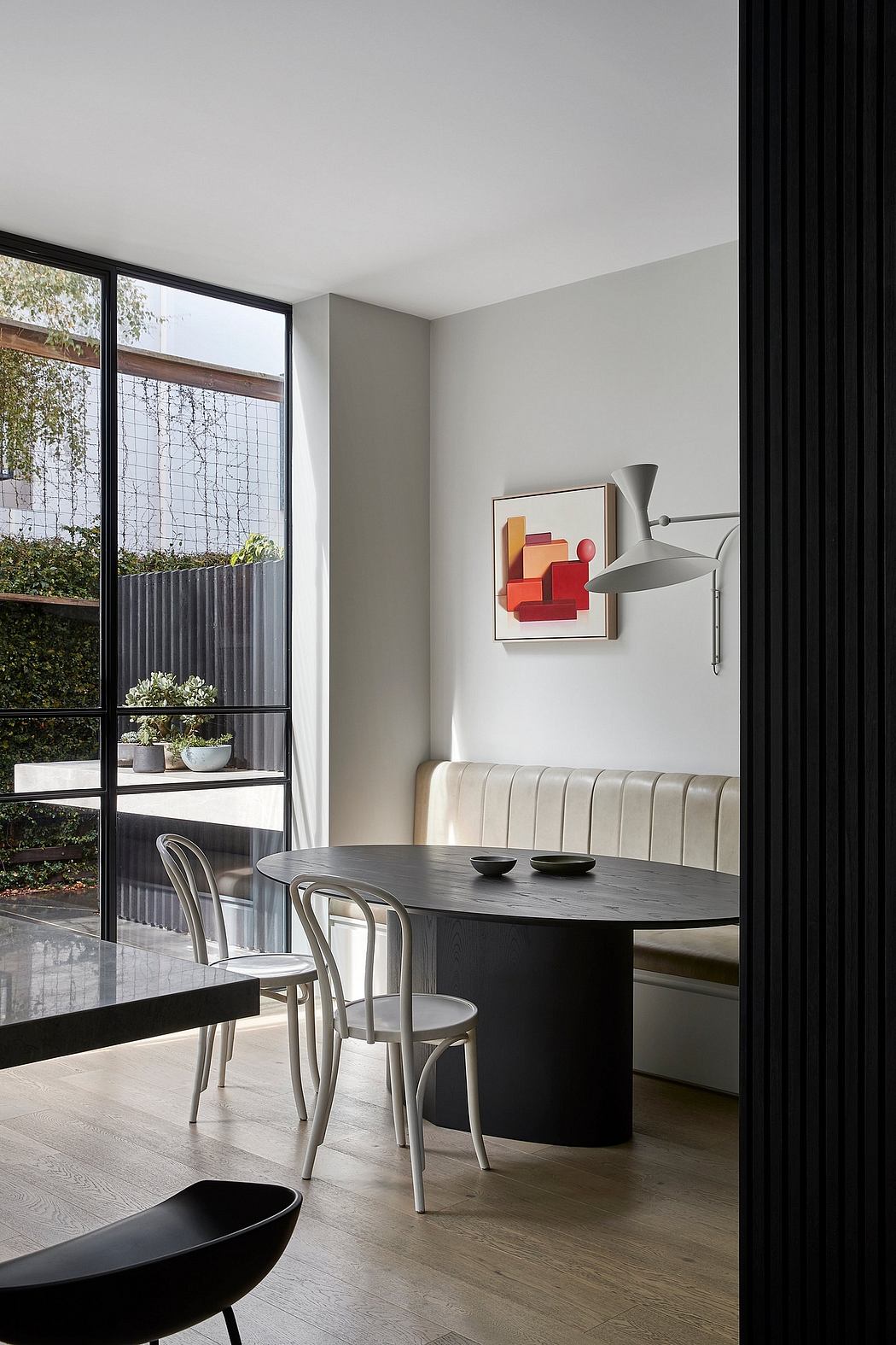 Contemporary dining area with sleek black table, vintage-style chairs, and vibrant abstract artwork.