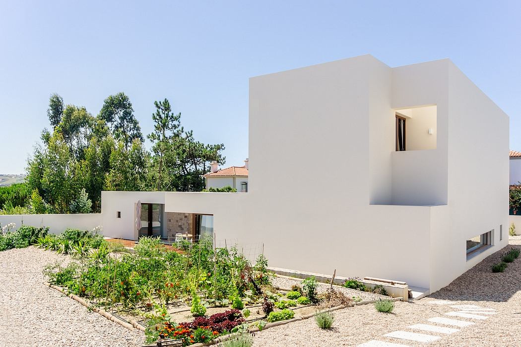 A modern white house with angular design, surrounded by a lush garden.