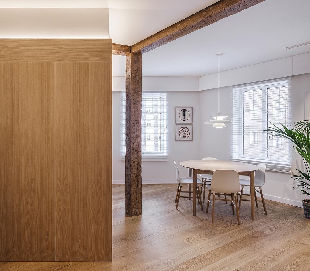 Bright, modern interior with exposed wooden beams, large windows, and a circular dining table.
