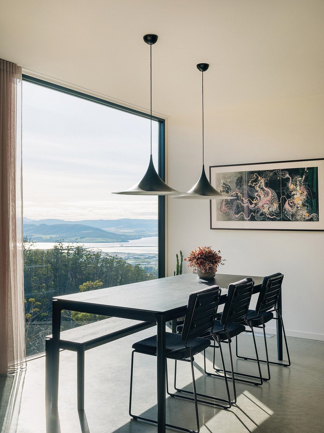 Modern dining space with striking pendant lighting, concrete floor, and scenic view.