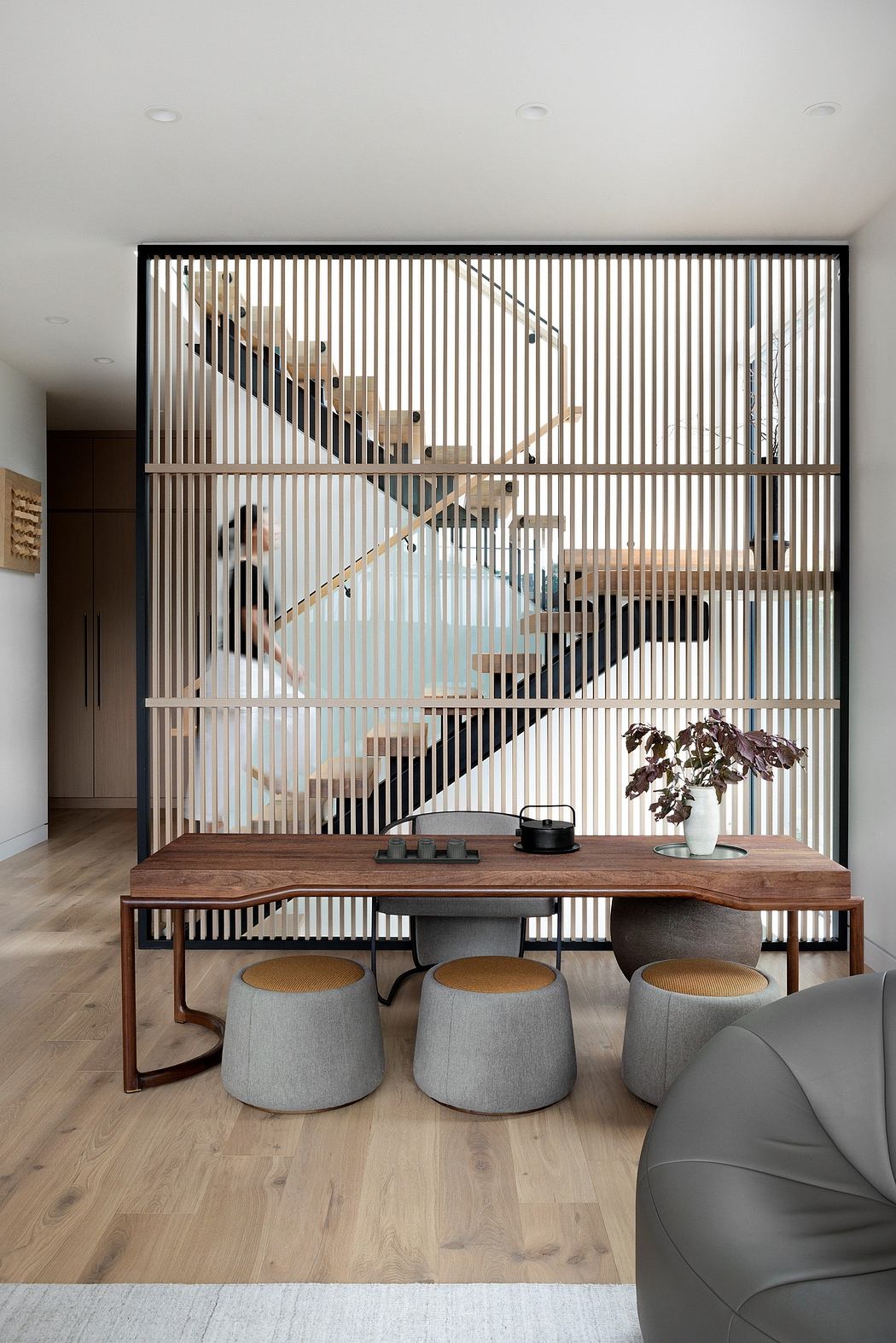 A modern living space with a wooden dining table, grey stools, and a striking slatted screen.