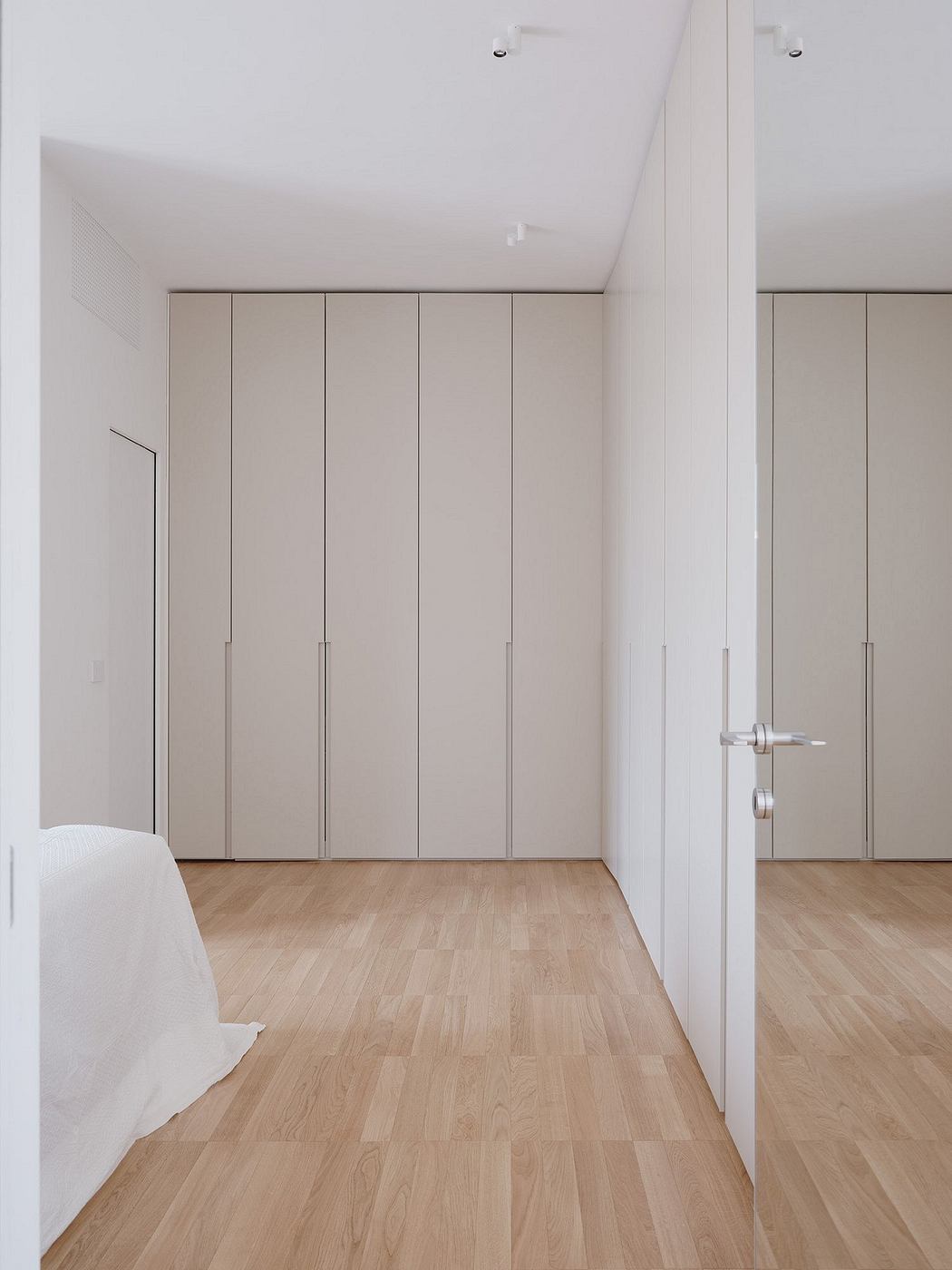 A minimalist bedroom with built-in closets and hardwood floors, showcasing clean lines and neutral tones.