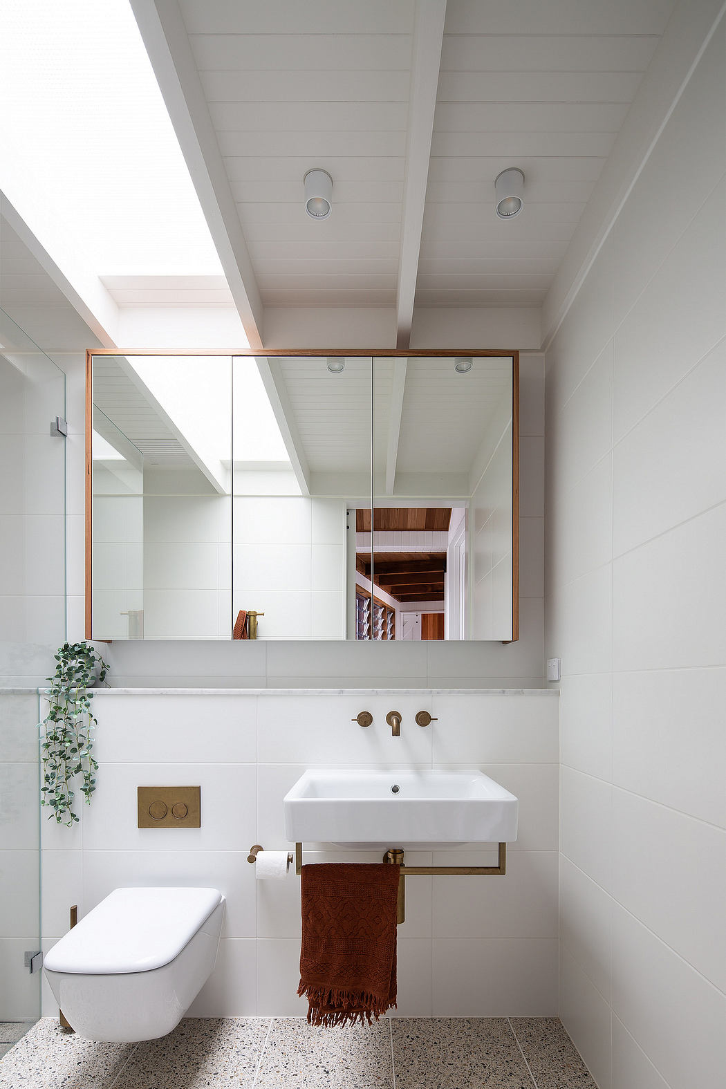 A minimalist bathroom with white walls, wood accents, and a floating vanity with a large mirror.