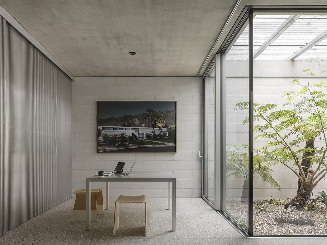 Minimalist concrete and glass interior with framed landscape photo and desk.