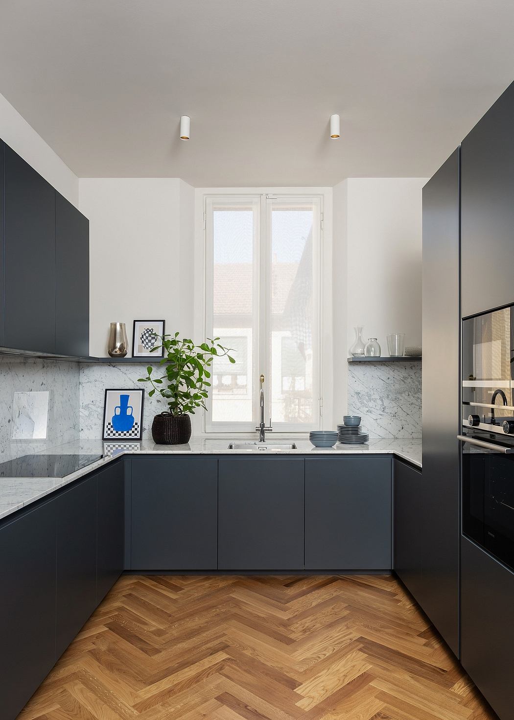 Sleek, modern kitchen with black cabinetry, marble backsplash, and herringbone wood flooring.