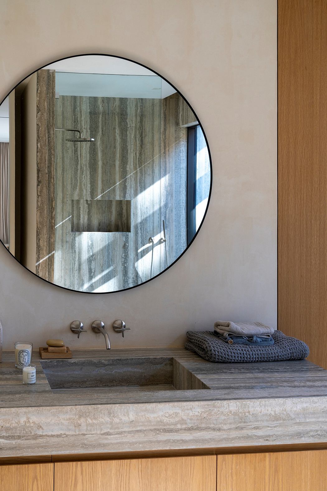 Circular mirror, stone vanity, and textured accents create a modern, spa-like bathroom.
