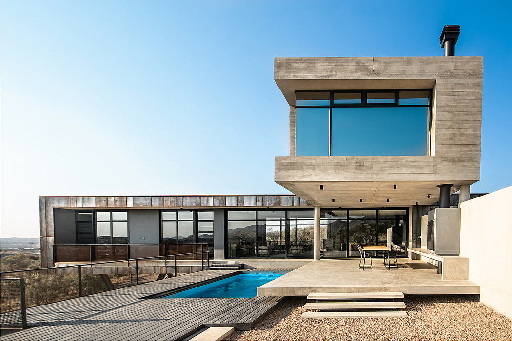 A modern concrete and glass structure with an inground pool and wooden deck, surrounded by a scenic landscape.