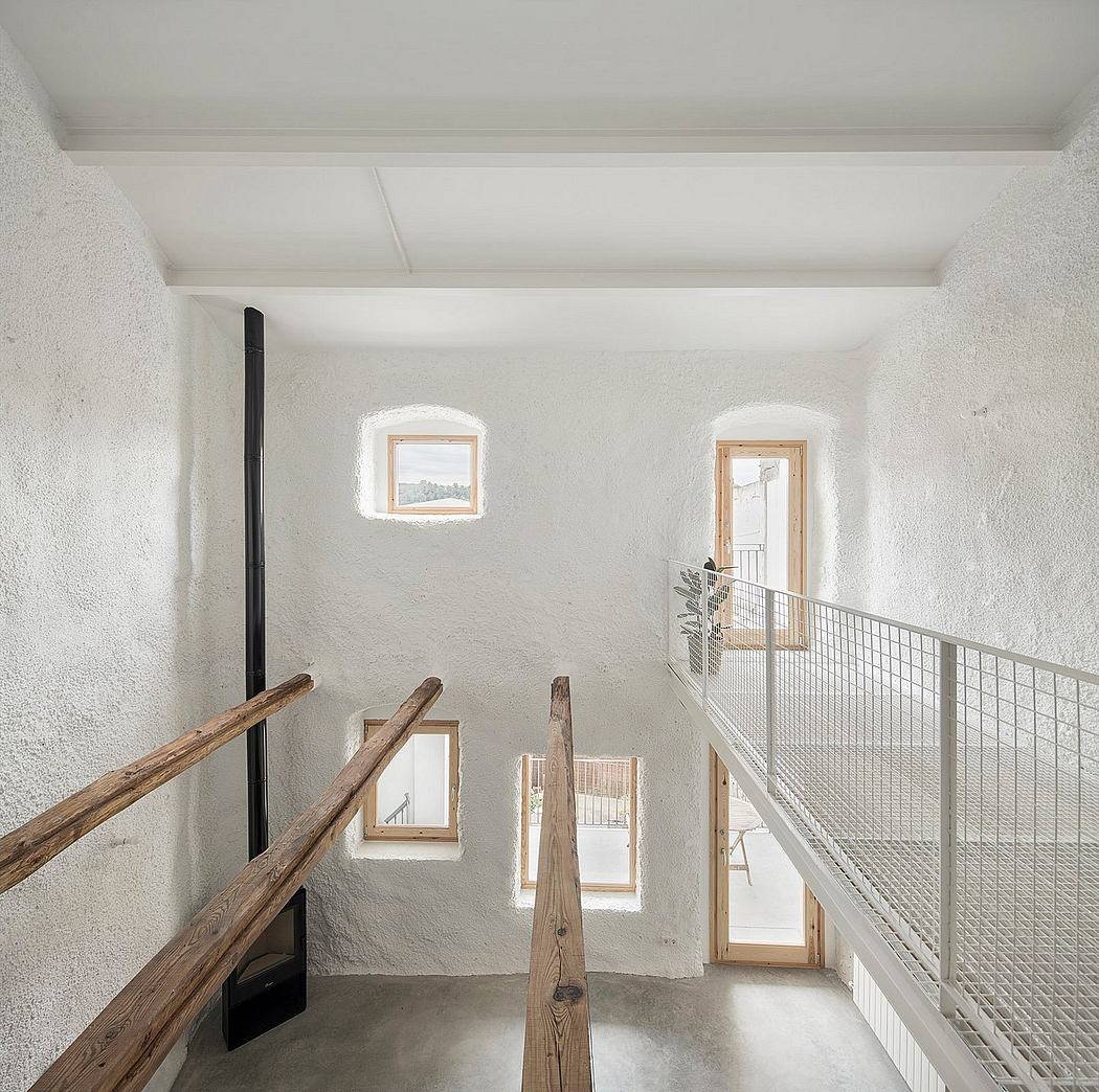 A minimalist interior with wood beams, wire railings, and arched windows.
