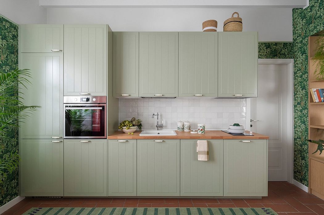 A minimalist kitchen design with light green cabinets, wooden countertops, and tropical-inspired wallpaper.