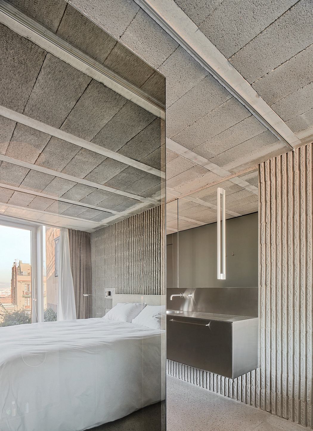 A modern, minimalist bedroom with a concrete ceiling and walls, stainless steel fixtures.