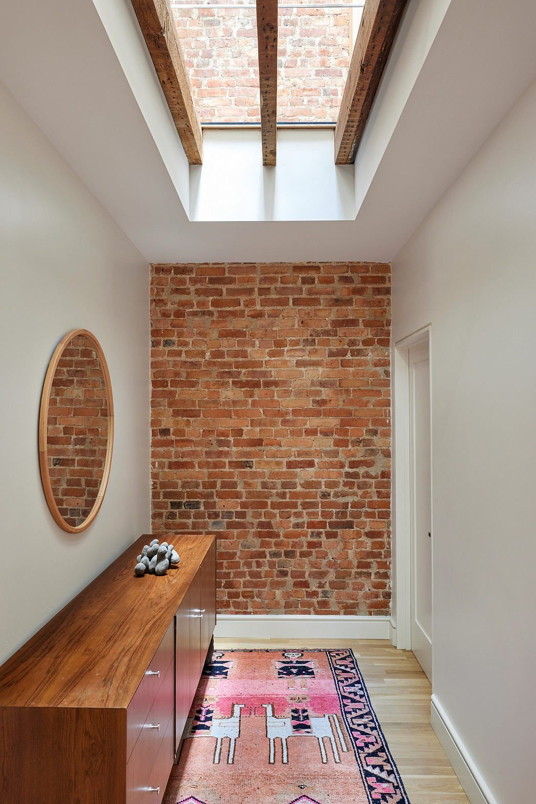 Spacious modern hallway with exposed brick walls, wooden bench, and vibrant patterned rug.