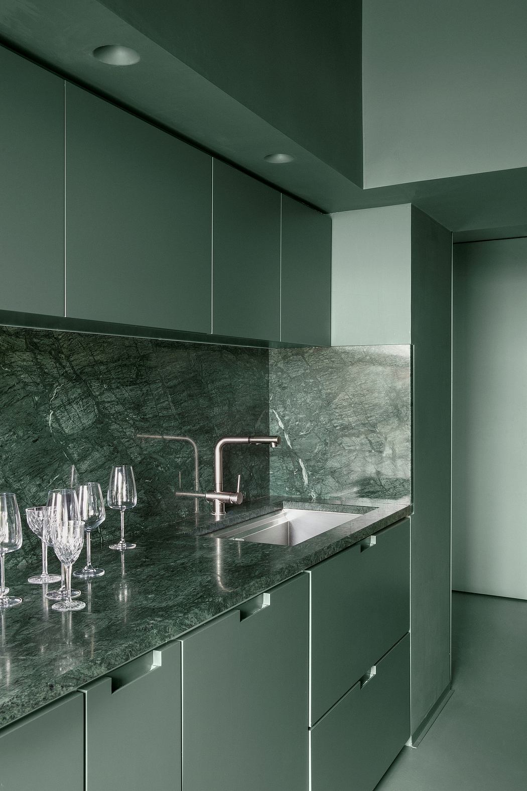 A modern kitchen with sleek green cabinets, a marble countertop, and a stainless steel sink.