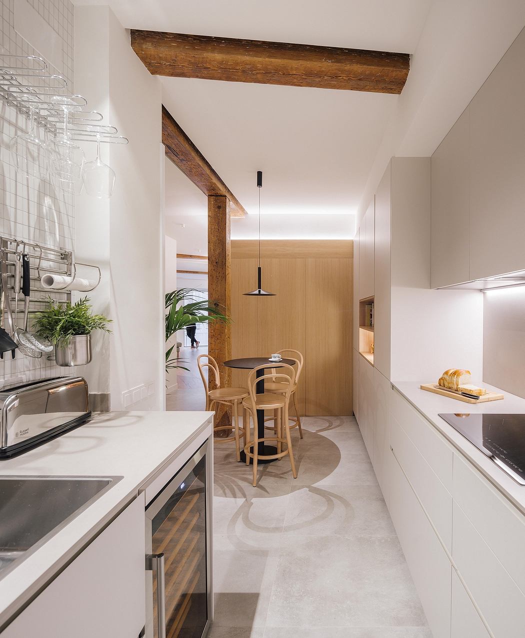 A modern kitchen with sleek white cabinets, wooden beams, and a cozy dining nook.